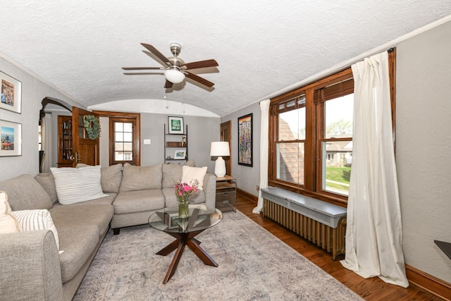 living area featuring radiator heating unit, a ceiling fan, baseboards, wood finished floors, and lofted ceiling