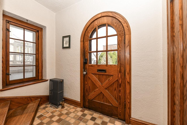 doorway to outside featuring radiator heating unit, baseboards, plenty of natural light, and a textured wall