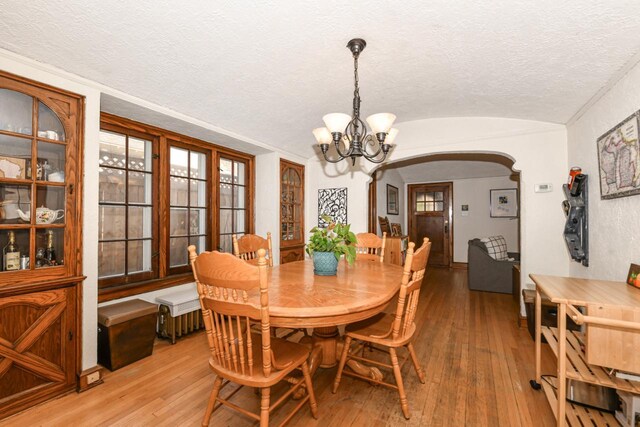 dining area featuring an inviting chandelier, a textured ceiling, arched walkways, light wood-style flooring, and vaulted ceiling