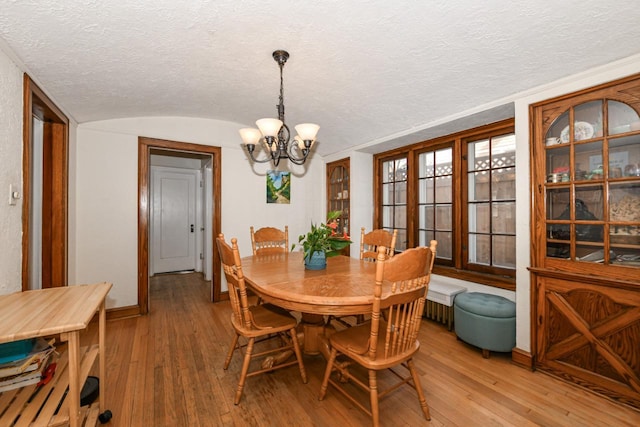 dining room with a notable chandelier, a textured ceiling, baseboards, light wood-type flooring, and vaulted ceiling