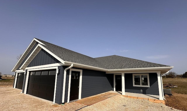 view of front of home with board and batten siding, driveway, cooling unit, an attached garage, and a shingled roof