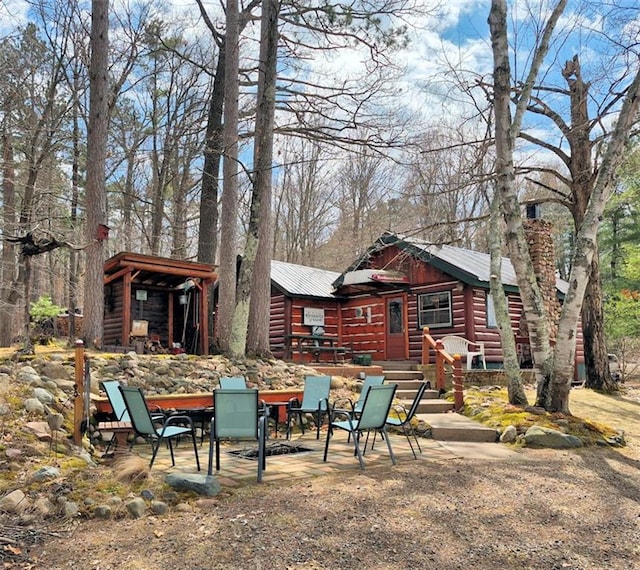 exterior space featuring outdoor dining space, a patio area, faux log siding, and metal roof
