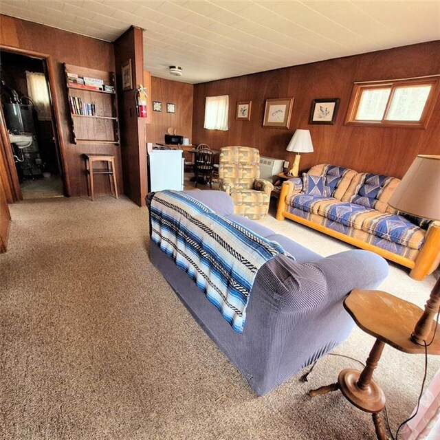 living room with carpet flooring, wooden walls, and water heater