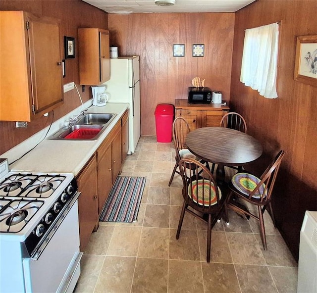 kitchen featuring wood walls, white appliances, light countertops, brown cabinets, and a sink