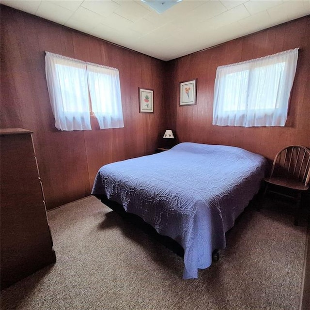bedroom with wooden walls, multiple windows, and carpet