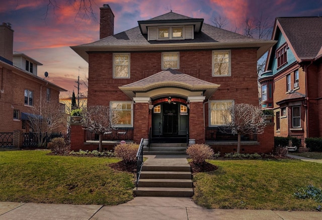 traditional style home with a lawn, brick siding, a chimney, and a shingled roof