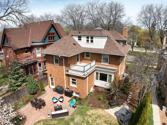 rear view of house with a balcony, a patio, roof with shingles, a chimney, and brick siding