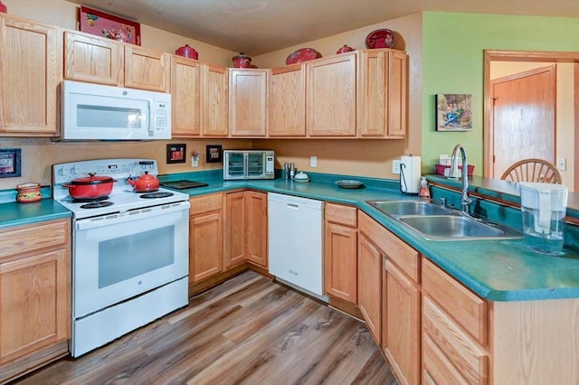 kitchen with light brown cabinetry, a sink, light wood-style floors, white appliances, and a peninsula