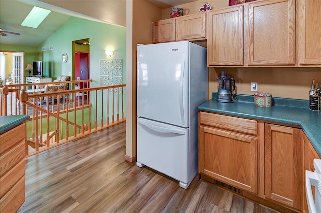 kitchen featuring visible vents, freestanding refrigerator, dark countertops, vaulted ceiling with skylight, and light wood-style flooring