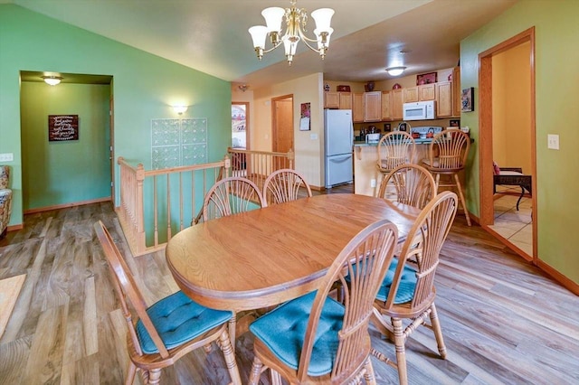 dining space with light wood-type flooring, baseboards, a chandelier, and vaulted ceiling