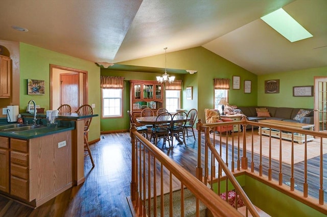 kitchen with dark countertops, lofted ceiling with skylight, dark wood-type flooring, a sink, and a notable chandelier