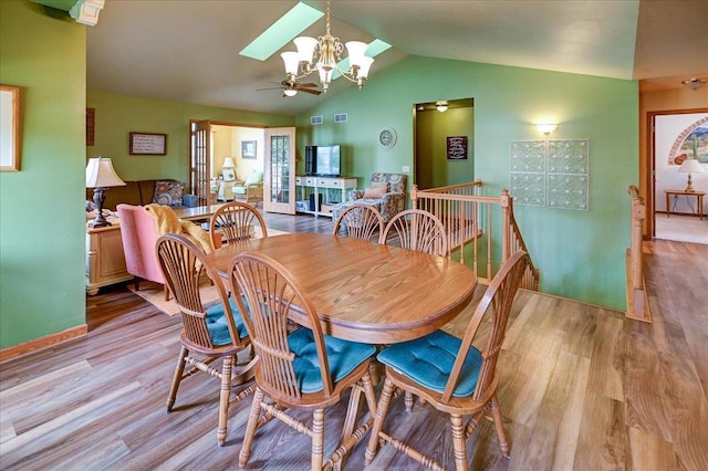 dining space with ceiling fan with notable chandelier, lofted ceiling with skylight, wood finished floors, and visible vents