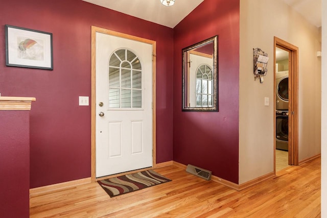foyer featuring baseboards, visible vents, stacked washer and clothes dryer, and light wood-type flooring