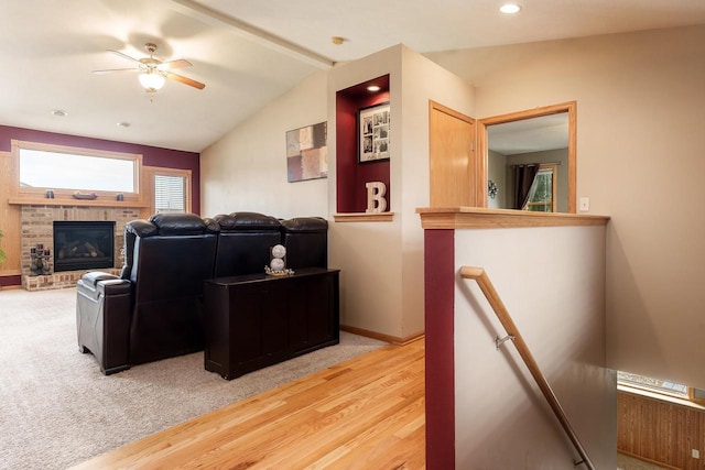 living area with baseboards, vaulted ceiling with beams, a ceiling fan, and a brick fireplace