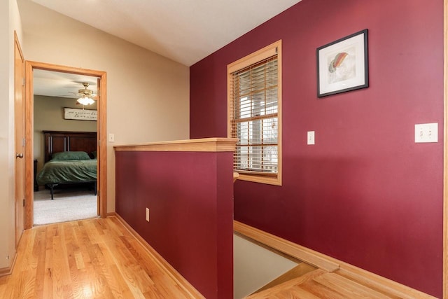 corridor featuring baseboards, wood finished floors, and an upstairs landing
