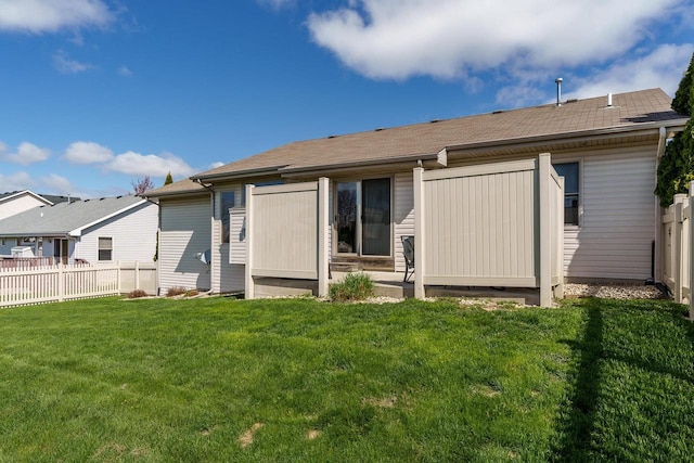 rear view of house with a lawn, fence, and roof with shingles