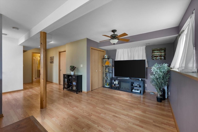 unfurnished living room with ceiling fan, baseboards, and light wood-type flooring