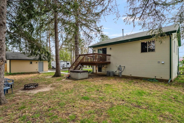 back of property with a lawn, a hot tub, a fire pit, and a wooden deck