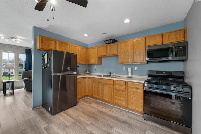 kitchen featuring ceiling fan, a sink, light countertops, freestanding refrigerator, and gas range