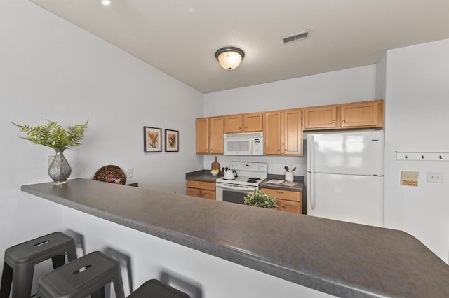 kitchen featuring dark countertops, a breakfast bar, white appliances, a peninsula, and visible vents