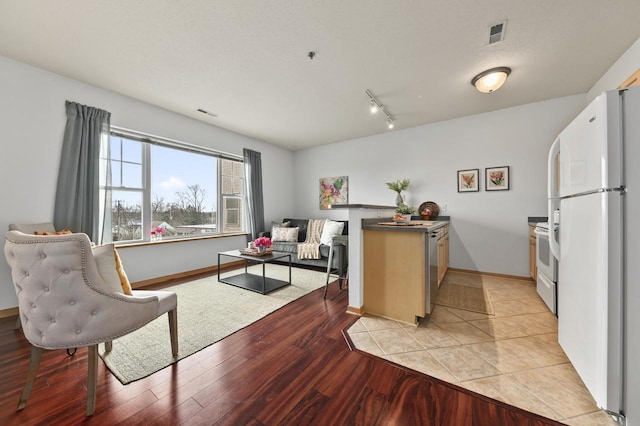 kitchen with visible vents, light wood-type flooring, rail lighting, baseboards, and white appliances