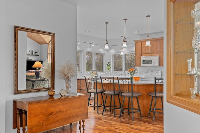 kitchen with a breakfast bar, stove, white microwave, light wood-style flooring, and hanging light fixtures