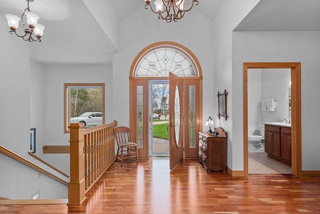 entryway with light wood-type flooring, baseboards, a chandelier, and vaulted ceiling