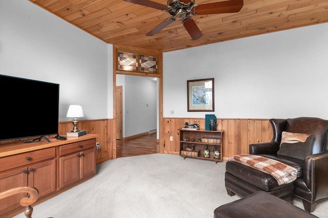 living room featuring a ceiling fan, wooden ceiling, a wainscoted wall, wooden walls, and light carpet