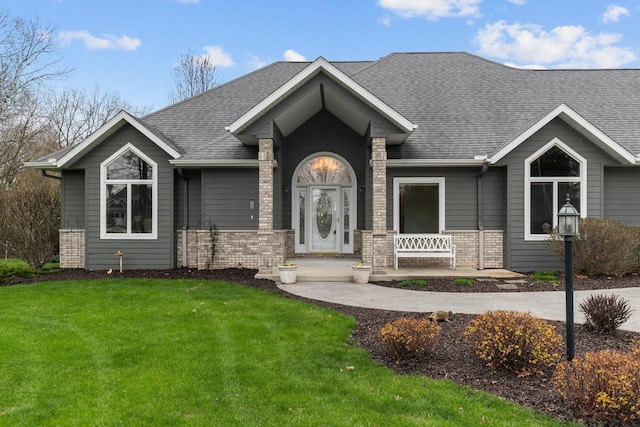 ranch-style home with a porch, brick siding, a shingled roof, and a front lawn