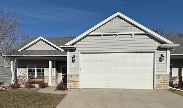 view of front of property featuring an attached garage, a shingled roof, driveway, and stone siding