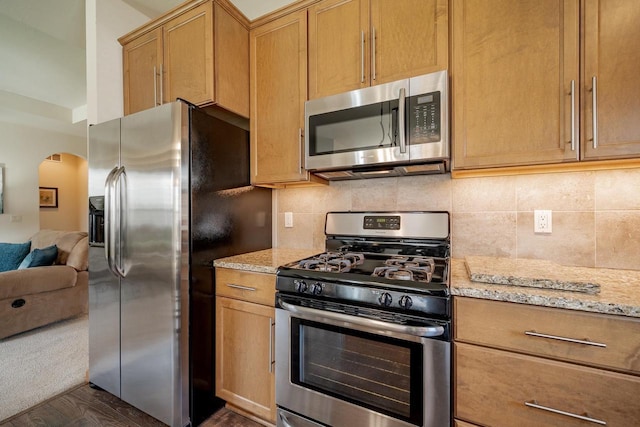kitchen featuring appliances with stainless steel finishes, light stone counters, arched walkways, open floor plan, and tasteful backsplash