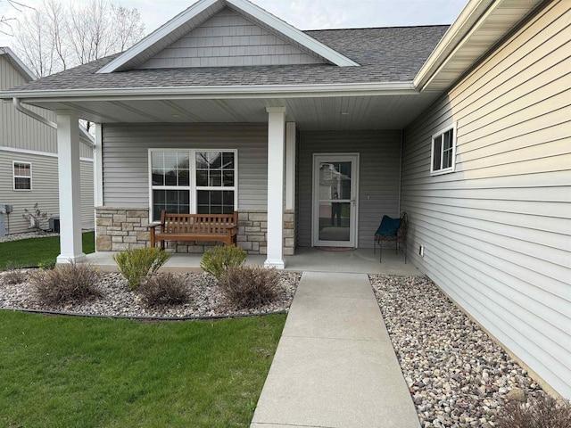 doorway to property with a shingled roof, a yard, a porch, and stone siding