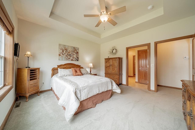 bedroom featuring ceiling fan, visible vents, light colored carpet, baseboards, and a raised ceiling