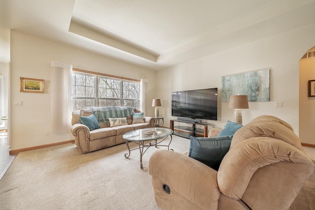 carpeted living room with arched walkways, baseboards, and a tray ceiling