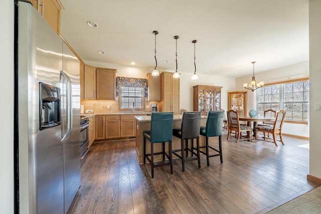 kitchen with appliances with stainless steel finishes, a kitchen breakfast bar, a chandelier, dark wood finished floors, and a center island