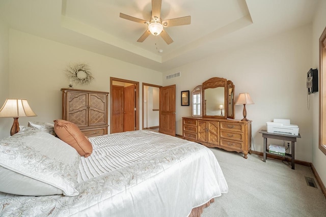 bedroom with visible vents, baseboards, a tray ceiling, and light colored carpet