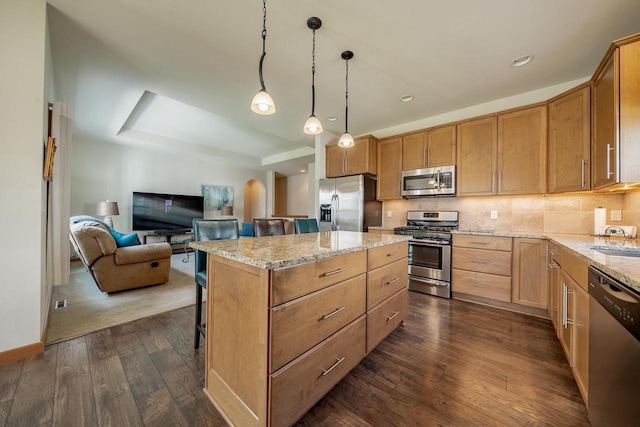 kitchen featuring a kitchen island, appliances with stainless steel finishes, dark wood finished floors, light stone counters, and a breakfast bar