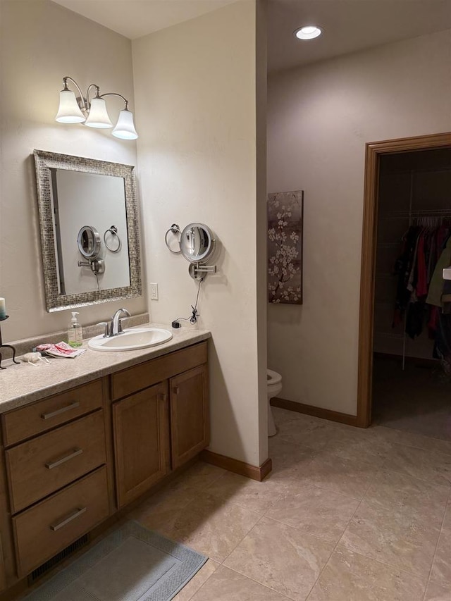 bathroom featuring a walk in closet, tile patterned flooring, vanity, toilet, and baseboards