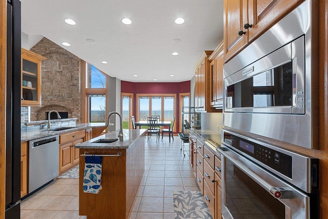 kitchen with a sink, appliances with stainless steel finishes, a kitchen island with sink, and light stone countertops
