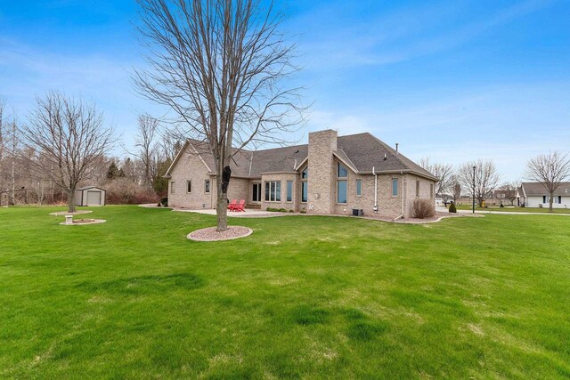 back of property with an outdoor structure, a chimney, a storage unit, brick siding, and a lawn