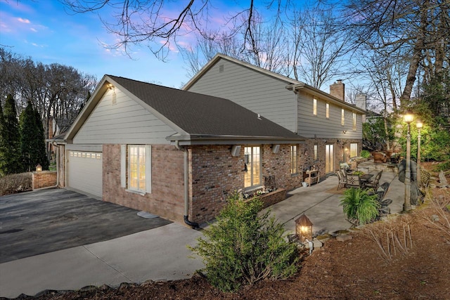 19425 Killarney Way, Brookfield, WI 53045 - property exterior at dusk featuring brick siding, a garage, aphalt driveway, and a chimney