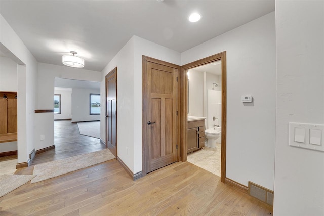 corridor with baseboards, light wood-style flooring, and visible vents