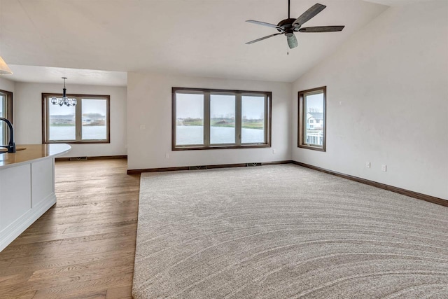 unfurnished living room with baseboards, ceiling fan with notable chandelier, wood finished floors, and vaulted ceiling