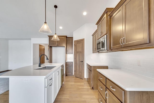 kitchen featuring tasteful backsplash, a sink, light wood-style flooring, appliances with stainless steel finishes, and decorative light fixtures