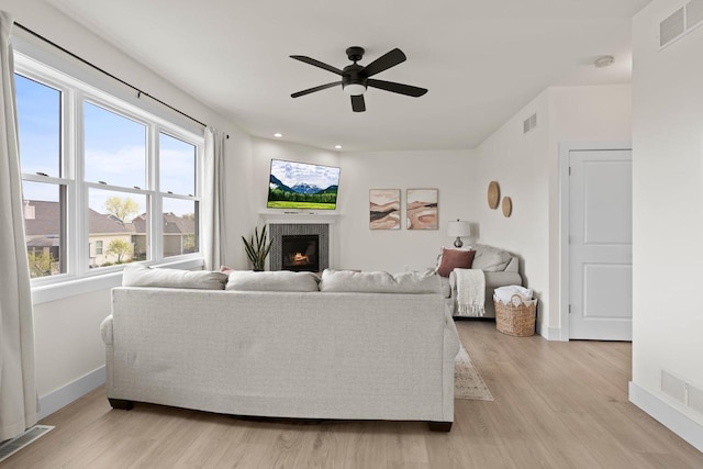 living area featuring light wood finished floors, ceiling fan, a lit fireplace, and baseboards