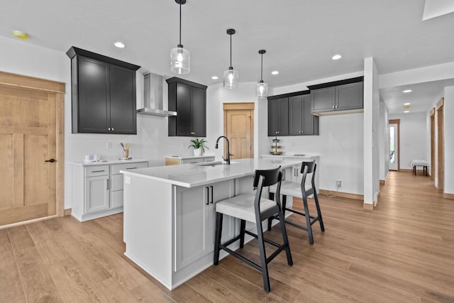 kitchen featuring light wood-style floors, an island with sink, recessed lighting, wall chimney exhaust hood, and a sink
