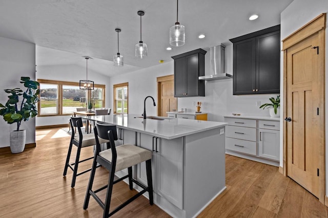 kitchen featuring a center island with sink, recessed lighting, wall chimney exhaust hood, a sink, and vaulted ceiling