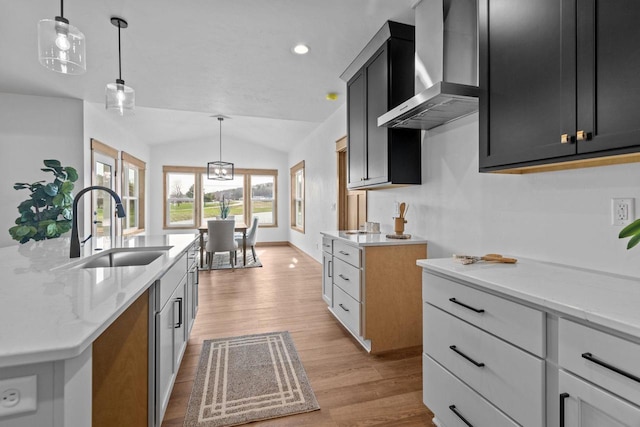 kitchen with wall chimney range hood, light stone countertops, a sink, lofted ceiling, and light wood-type flooring