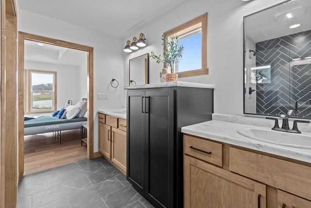 full bathroom featuring two vanities, a tile shower, and a sink
