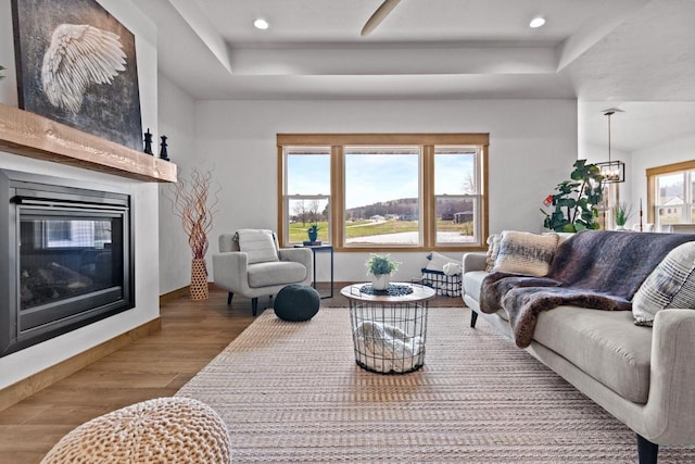 living area featuring a glass covered fireplace, a tray ceiling, recessed lighting, and wood finished floors